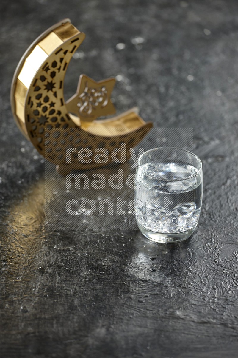 A wooden golden crescent lantern with different drinks, dates, nuts, prayer beads and quran on textured black background