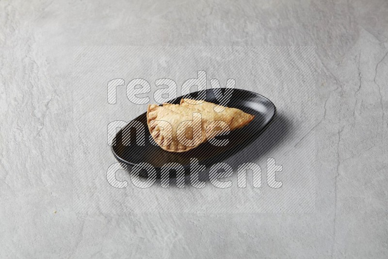 Three fried sambosas in an oval shaped black plate on a gray background
