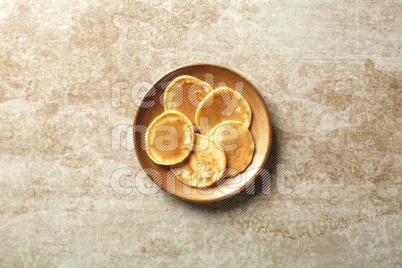 Five stacked plain mini pancakes in a brown plate on beige background