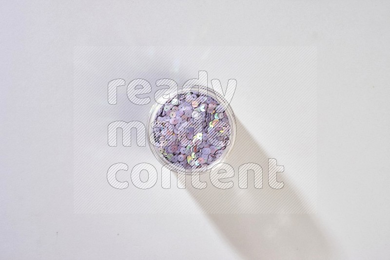 A glass jar full of colored sequins on grey background