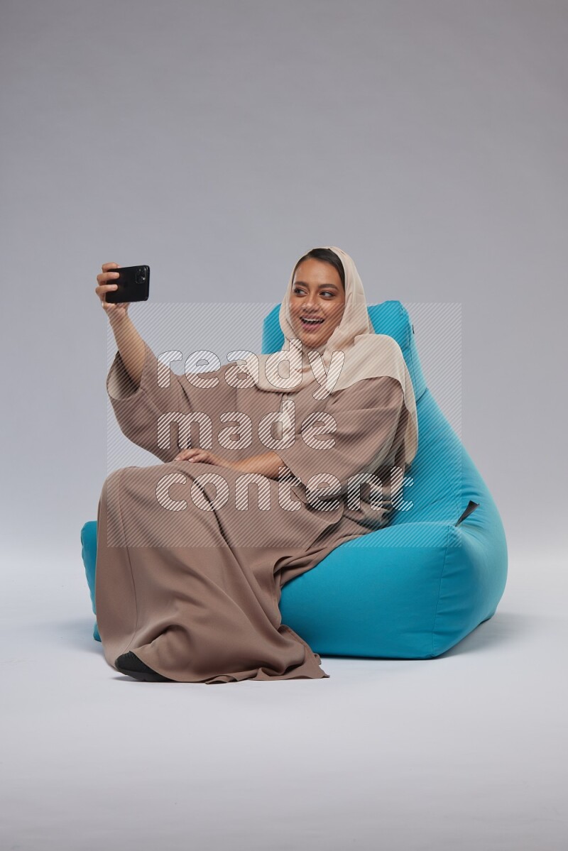 A Saudi woman sitting on a blue beanbag and taking selfie