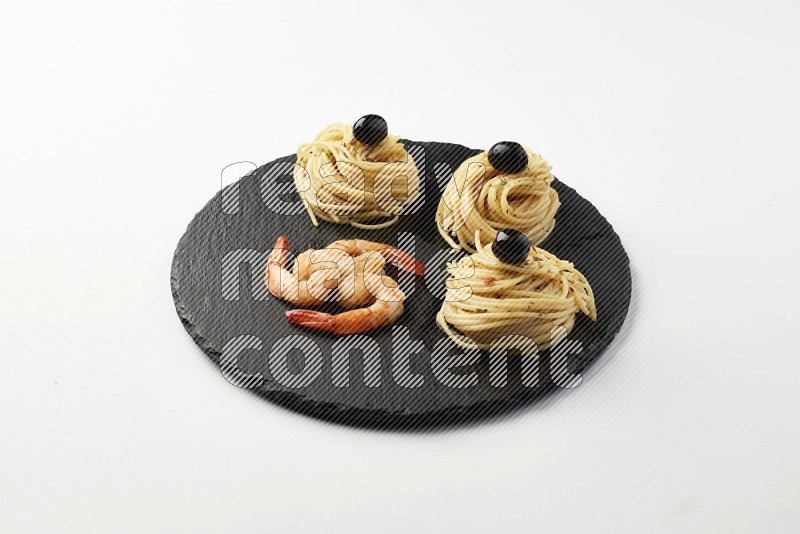spaghetti nests with white sauce and shrimp on a black slate on a white background