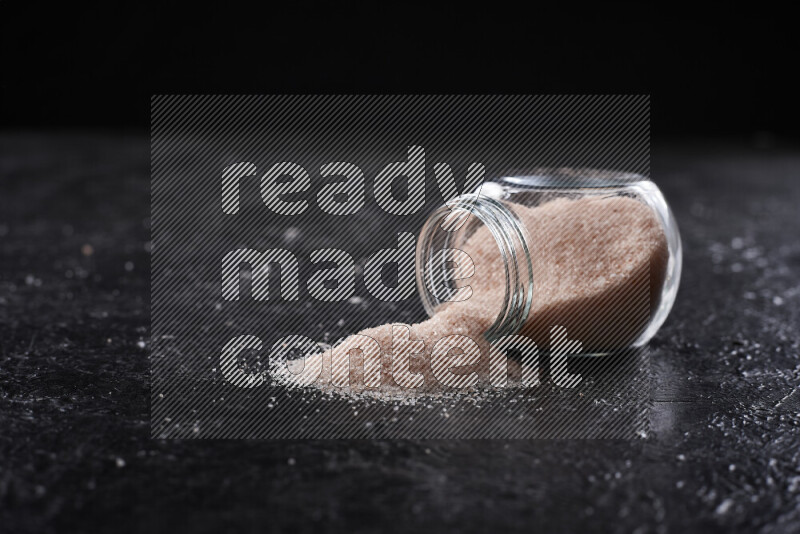 A glass jar full of fine himalayan salt on black background