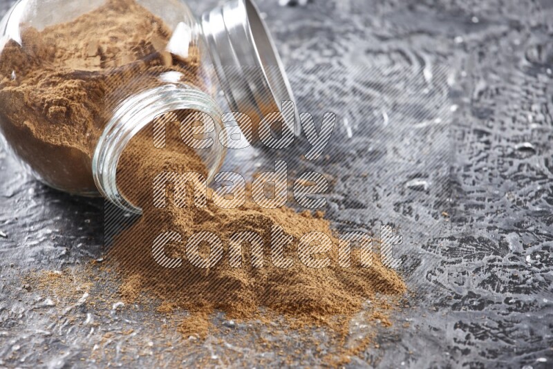 Flipped herbal glass jar full of cinnamon powder on textured black background
