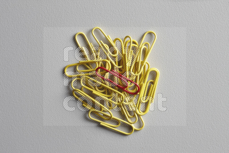 A bunch of yellow paper clips with a different colored paper clip in the center on grey background