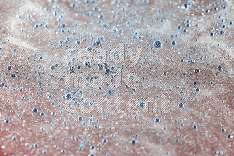 لقطات مقربة لقطرات ألوان مائية زرقاء على سطح الزيت على خلفية حمراء