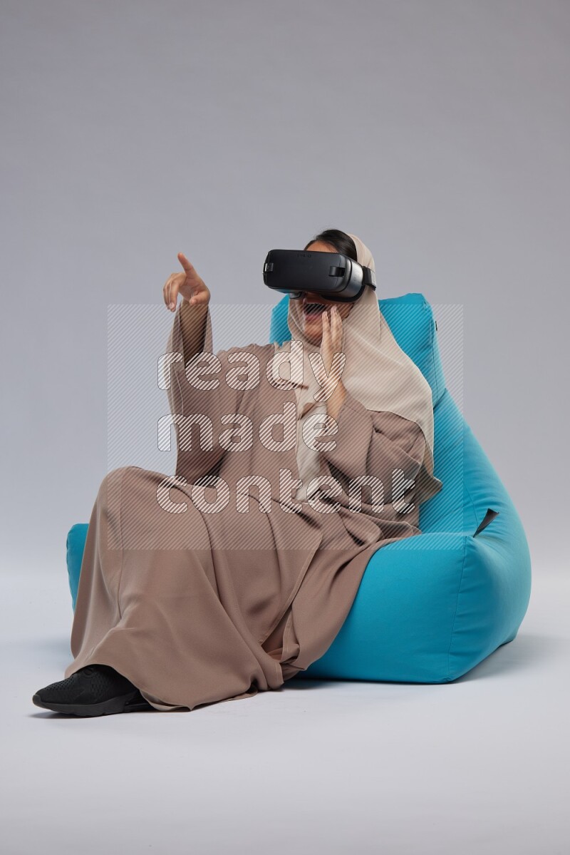 A Saudi woman sitting on a blue beanbag and gaming with VR