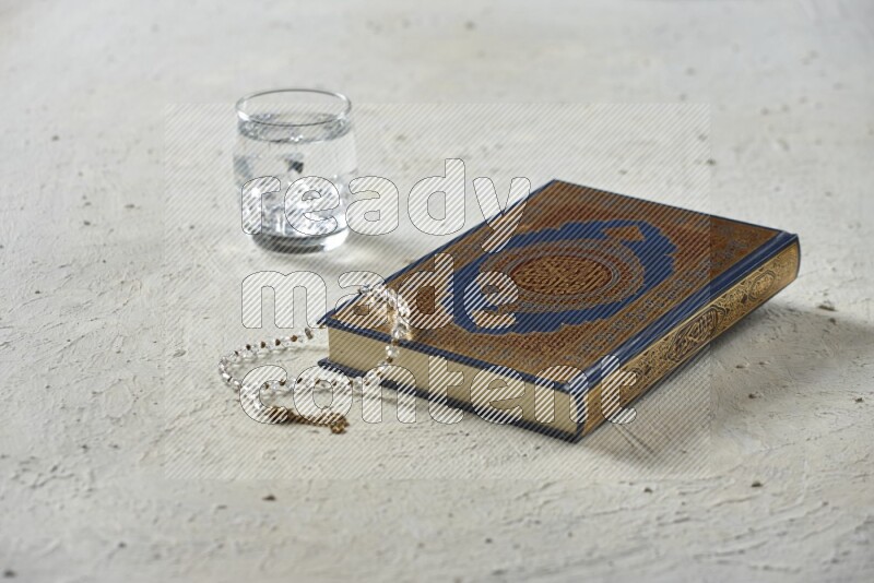Quran with dates, prayer beads and different drinks all placed on textured white background