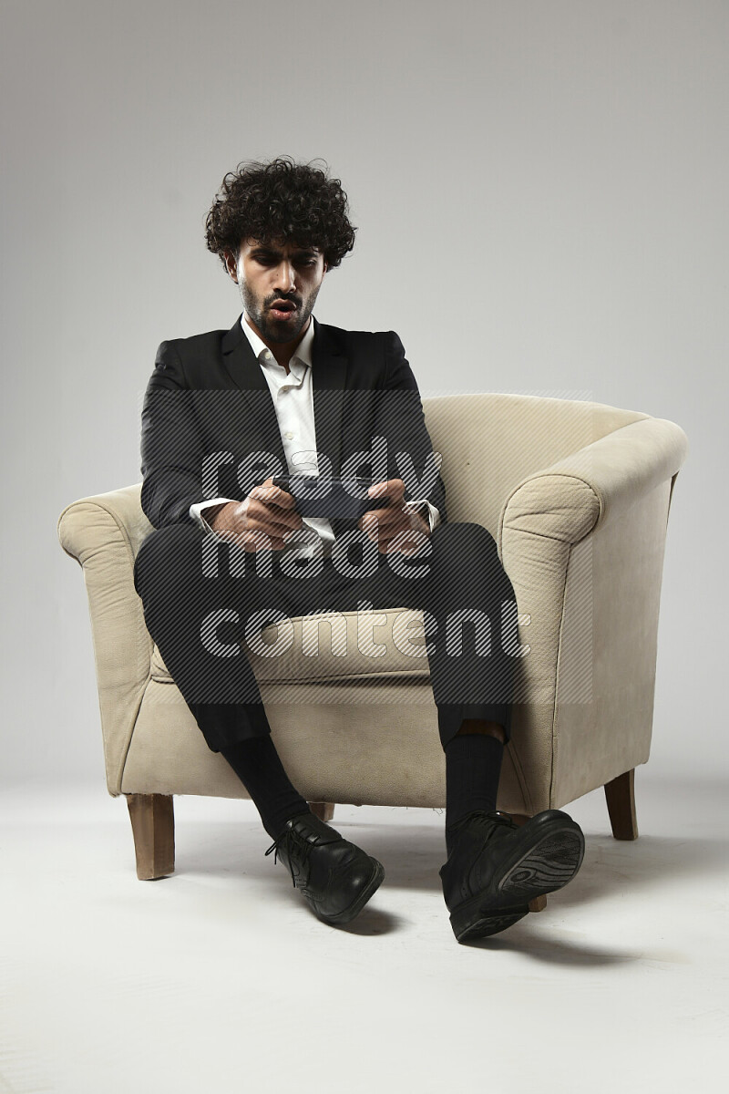 رجل يرتدي ملابس رسمية يجلس علي كرسي و يلعب علي الهاتف علي خلفية بيضاء
