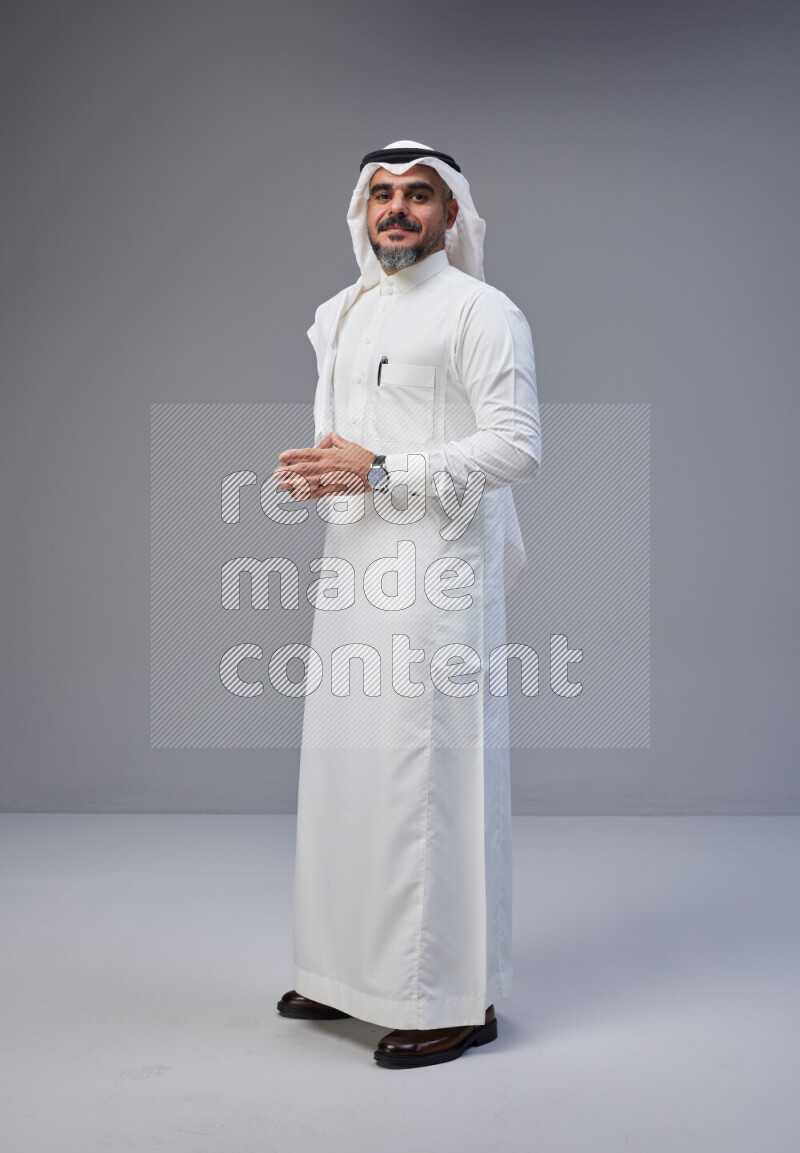Saudi man Wearing Thob and white Shomag standing interacting with the camera on Gray background