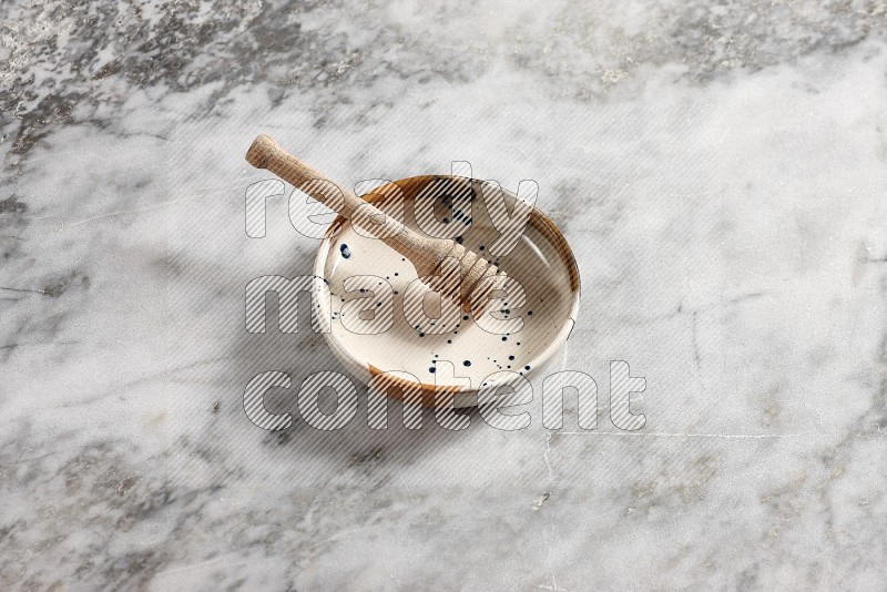 Multicolored Pottery bowl with wooden honey handle in it, on grey marble flooring, 65 degree angle