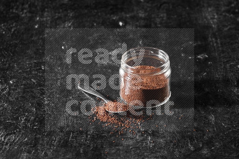 A glass jar full of garden cress and a metal spoon full of the seeds on a textured black flooring in different angles