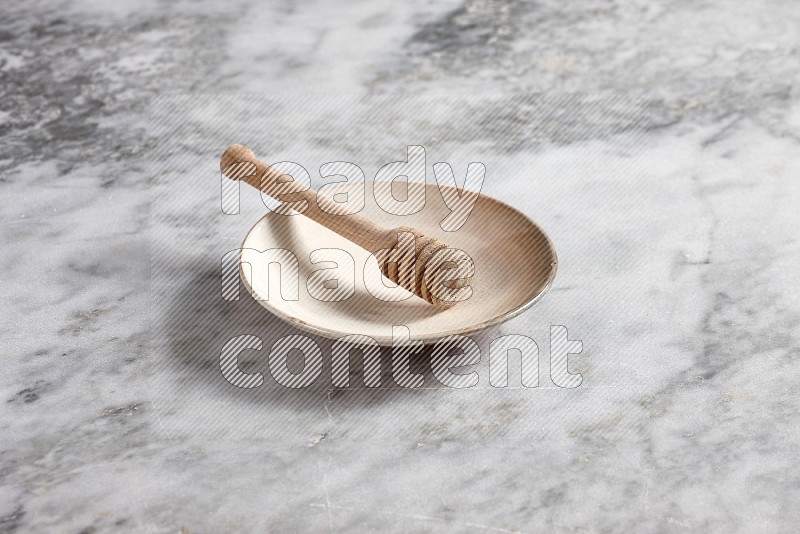Beige Pottery Plate with wooden honey handle in it, on grey marble flooring, 45 degree angle