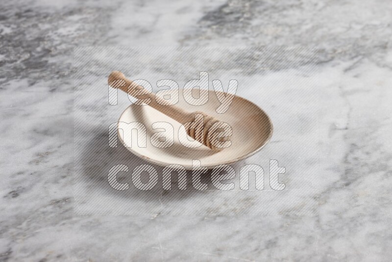 Beige pottery plate with wooden honey dipper in it on grey marble background