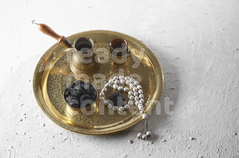 Dried plums in a metal bowl with coffee and prayer beads on a tray in a light setup