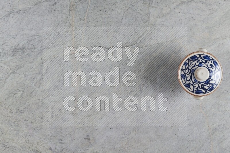 A multicolored pottery pot with its lid on grey marble background