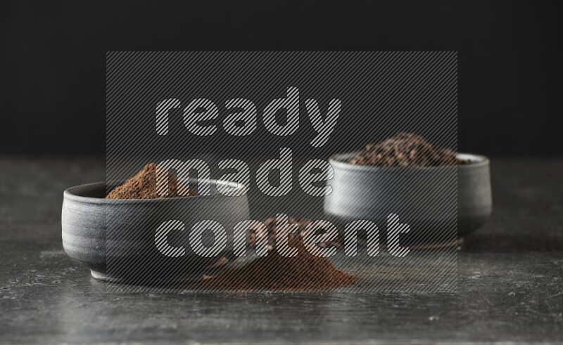 وعاءين من الفخار الأسود أحدهما ممتلئي بحبوب القرنفل والآخر ممتلئ ببودرة القرنفل على خلفية سوداء