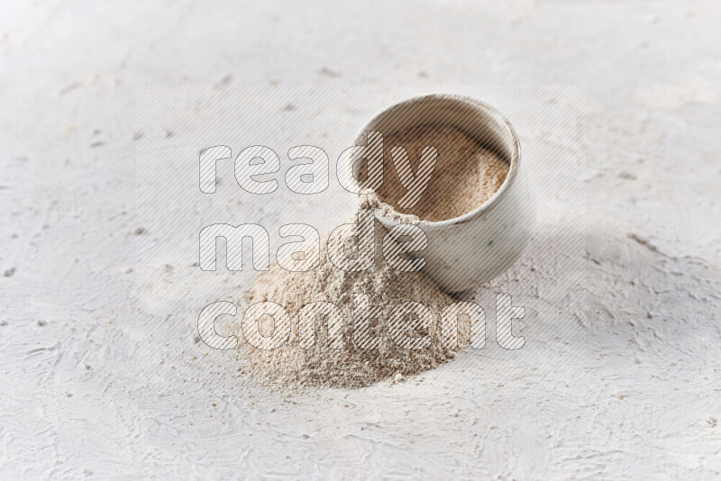 A beige pottery bowl full of onion powder with fallen powder from it on white background