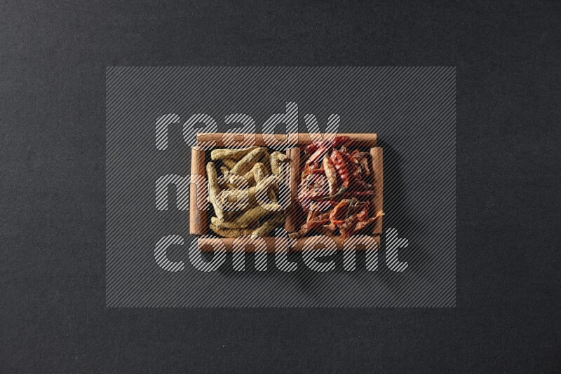 مربعان من أعواد القرفة ممتلئان بالفلفل الحار المجفف وأصابع الكركم علي خلفية سوداء