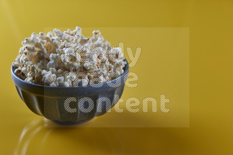 A blue pottery bowl full of popcorn on a yellow background in different angles