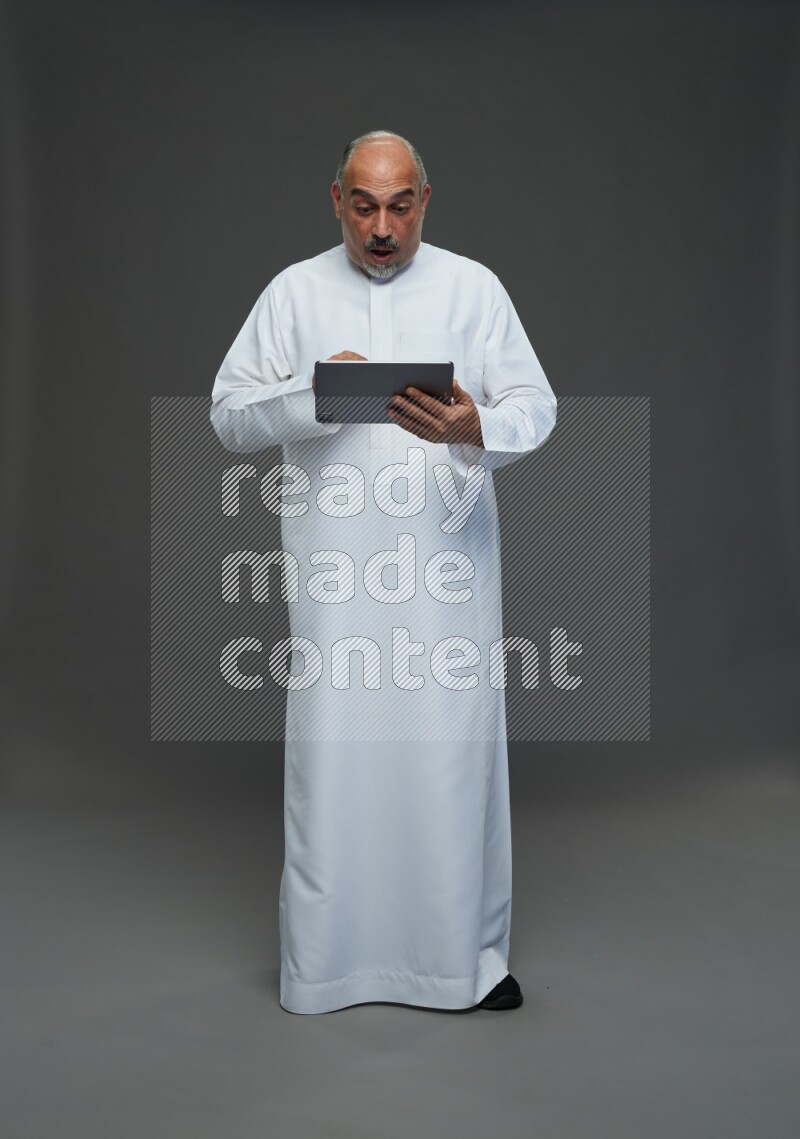 Saudi man without shomag Standing working on tablet on gray background