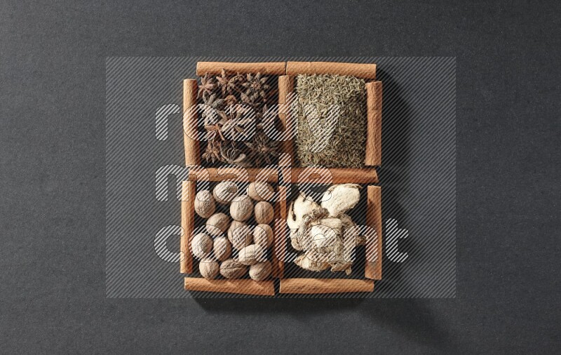 4 مربعات من عيدان القرفة ممتلئة باليانسون النجمي والكمون والزنجبيل المجفف وجوزة الطيب على أرضية سوداء