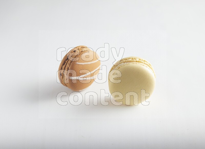 45º Shot of of two assorted Brown Irish Cream, and Yellow Vanilla macarons on white background