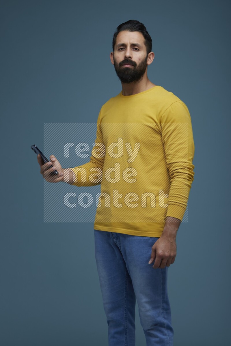 Man posing with a phone in a blue background wearing a yellow shirt