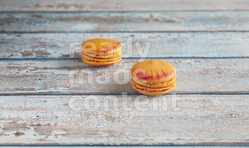 45º Shot of two orange Exotic macarons on light blue wooden background