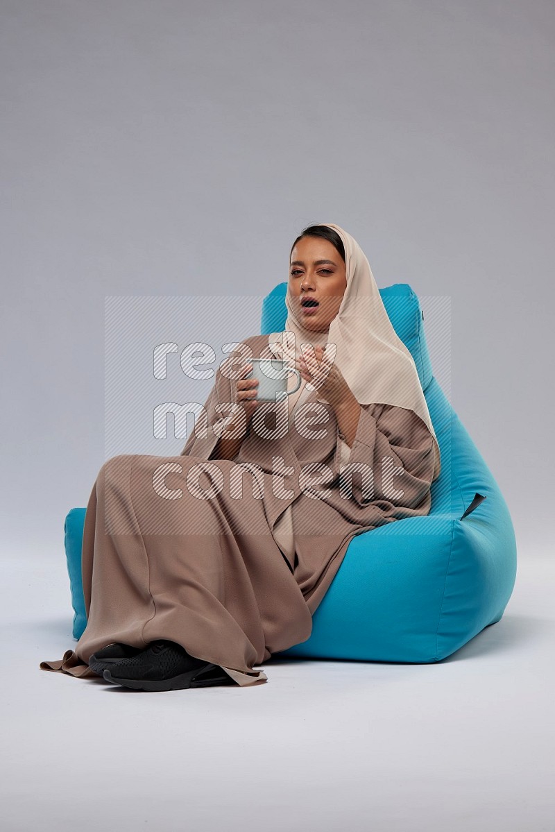 A Saudi woman sitting on a blue beanbag and drinking coffee