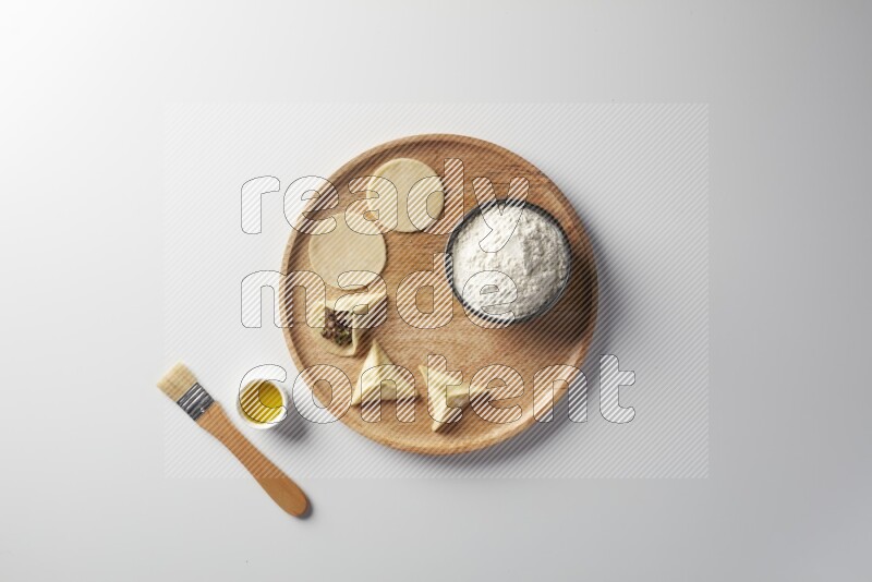 two closed sambosas and one open sambosa filled with meat while flour, and oil with oil brush aside in a wooden dish on a white background