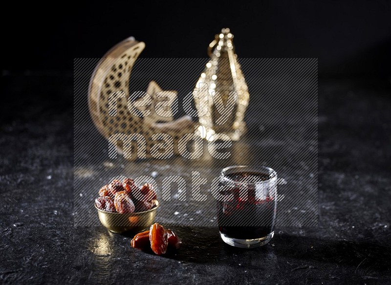 Dates in a metal bowl and tamarand beside a gold crescent and a lantern in a dark setup