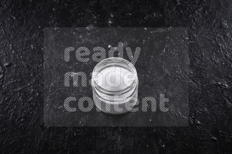 A glass jar full of fine table salt on black background