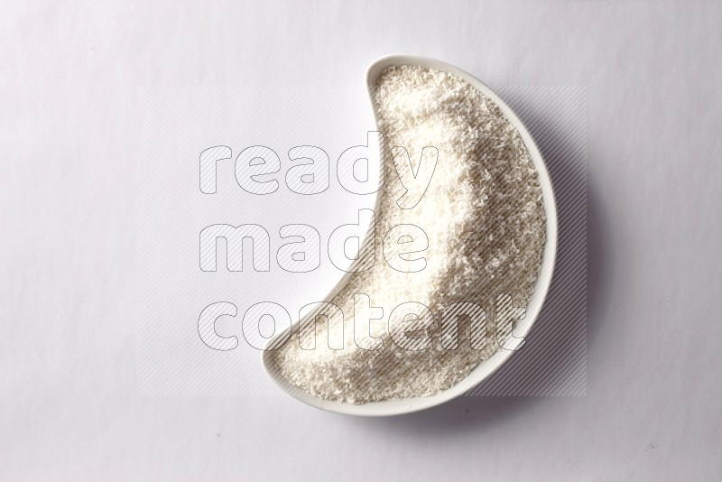 Desiccated coconuts in a crescent pottery plate on white background