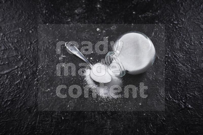 A glass jar full of fine table salt on black background