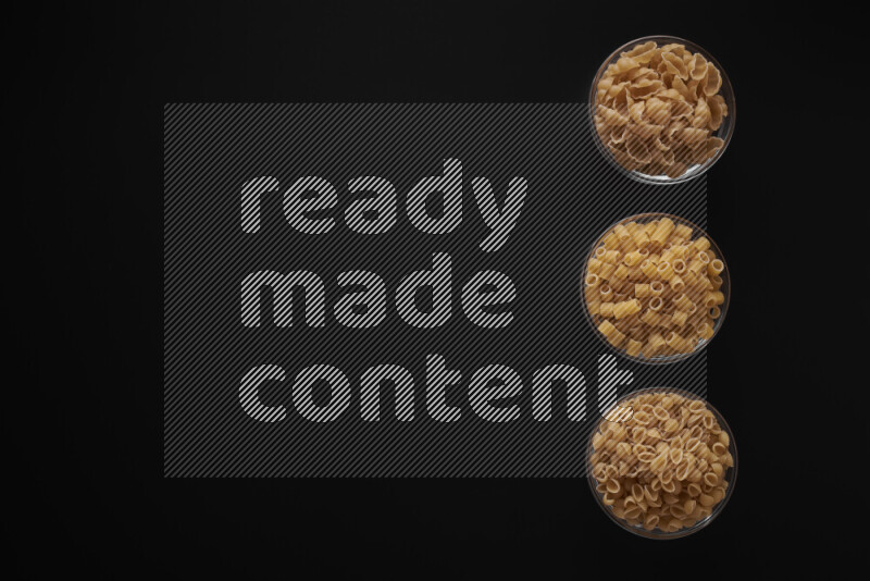 Different pasta types in 3 glass bowls on black background
