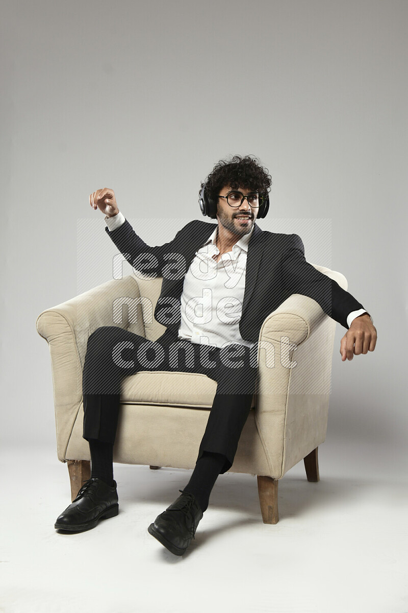 A man wearing formal sitting on a chair putting on headphones on white background