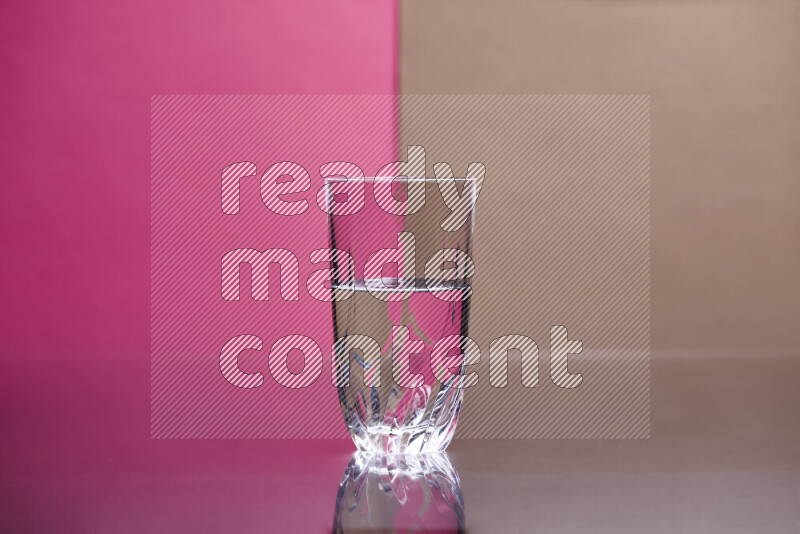 The image features a clear glassware filled with water, set against pink and beige background