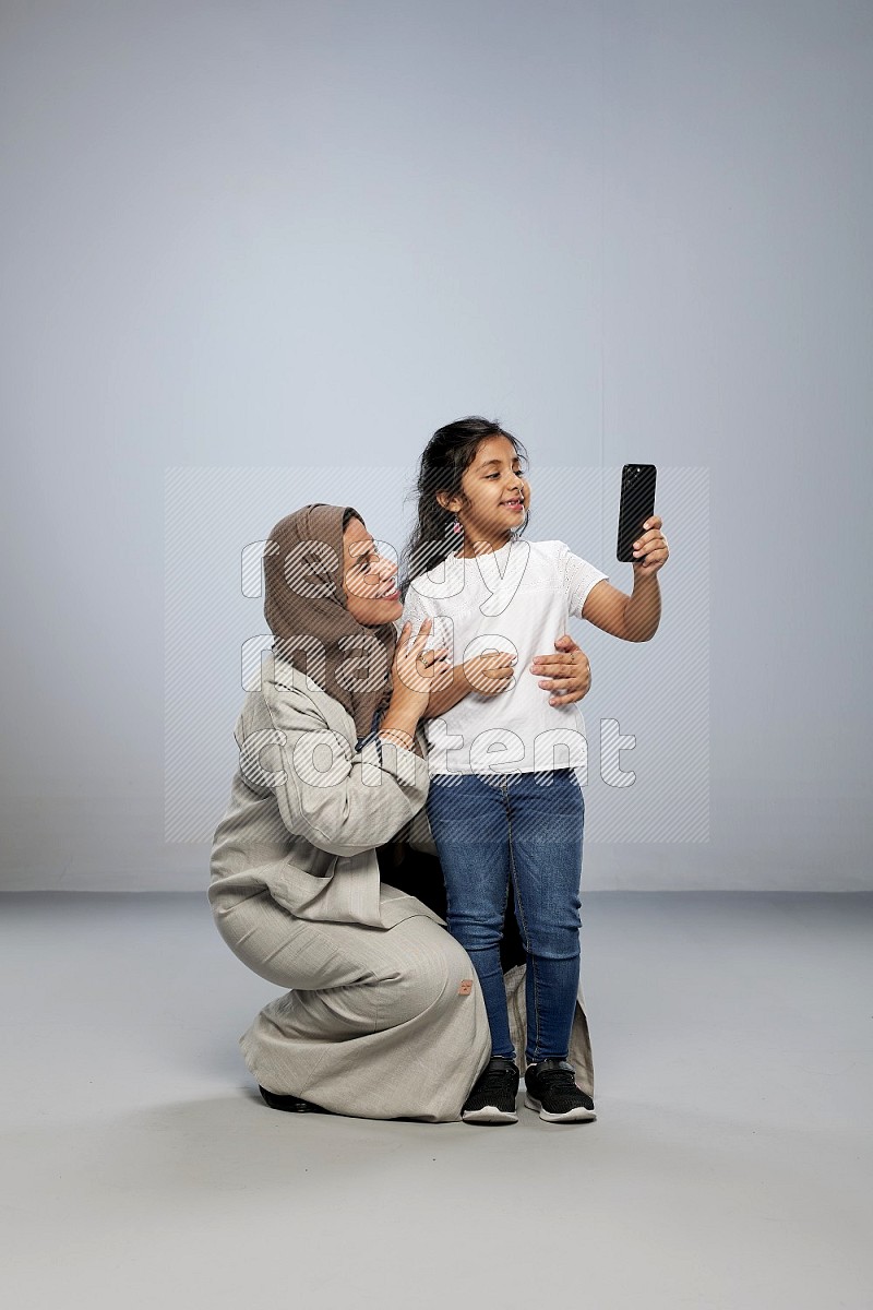 A girl standing taking selfie with her mother on gray background