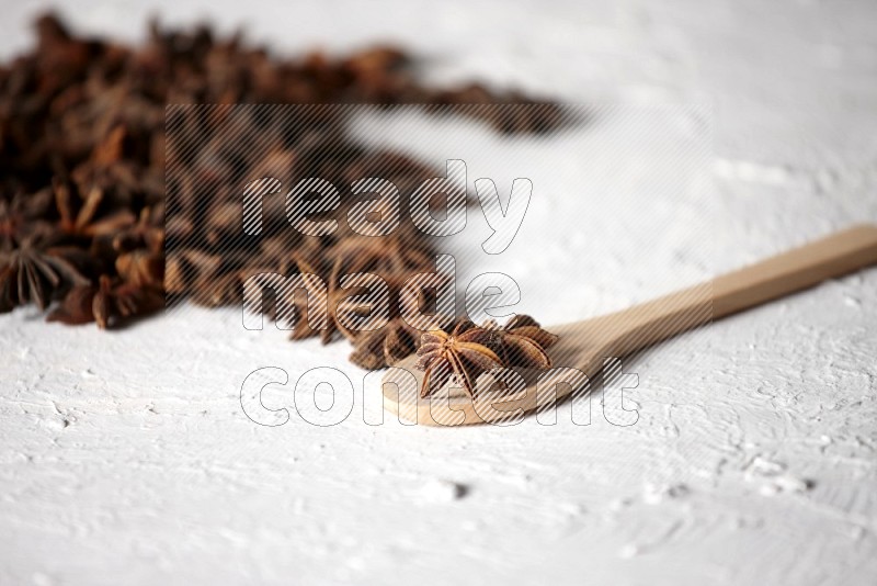 Star anise on a wooden spoon and spreading on the background on a white flooring