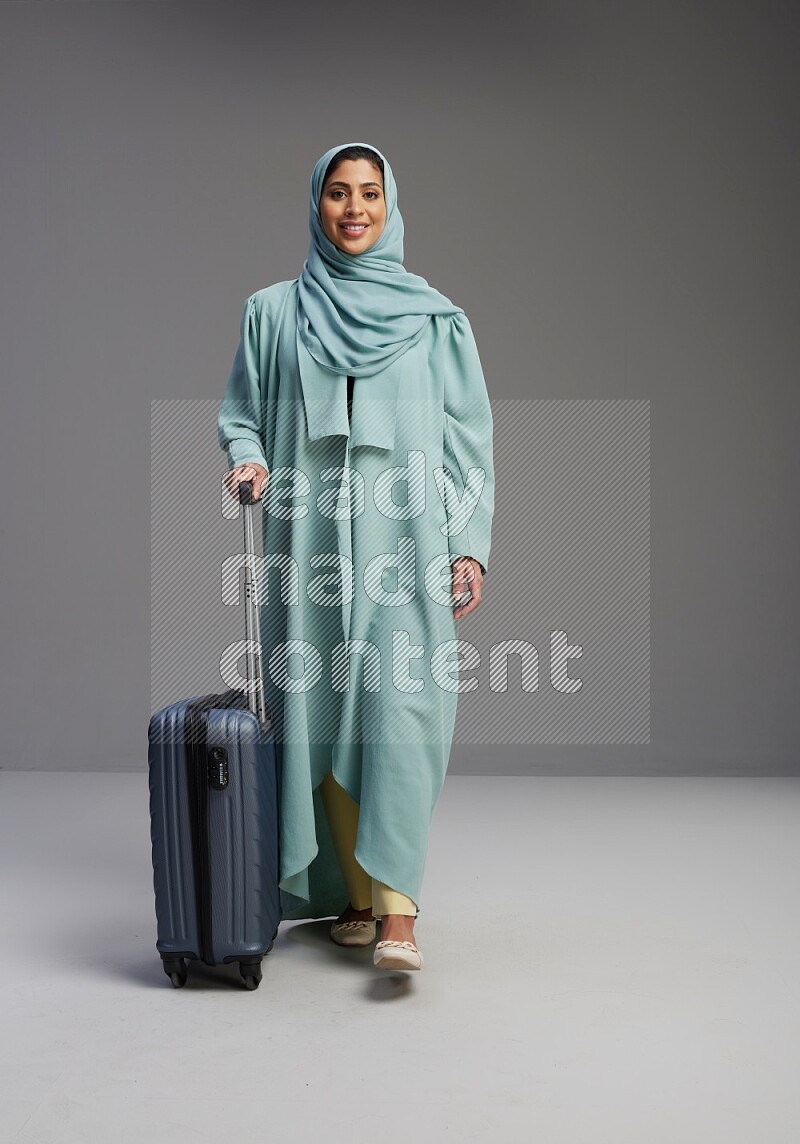 Saudi Woman wearing Abaya standing holding Travel bag on Gray background