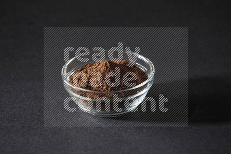 A glass bowl full of cloves powder on black flooring