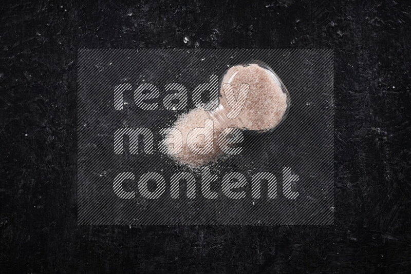 A glass jar full of fine himalayan salt on black background