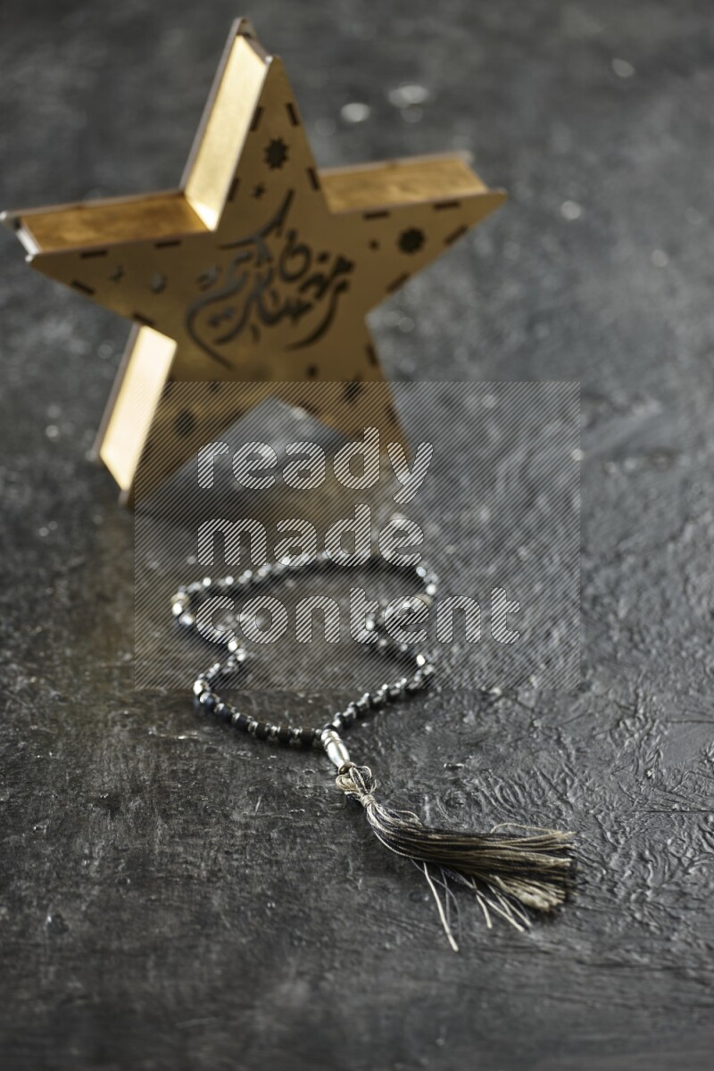 A wooden golden star lantern with different drinks, dates, nuts, prayer beads and quran on textured black background