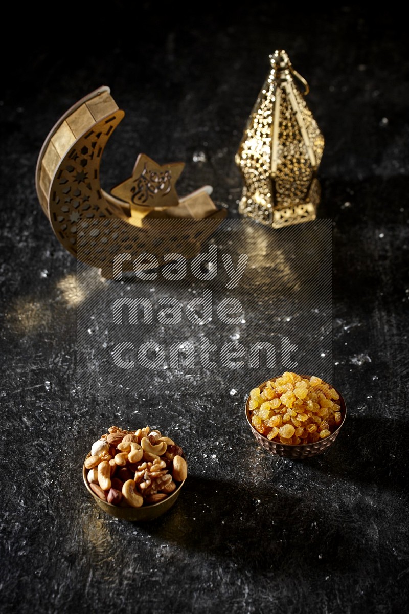 Nuts in a metal bowl with raisins beside golden lanterns in a dark setup