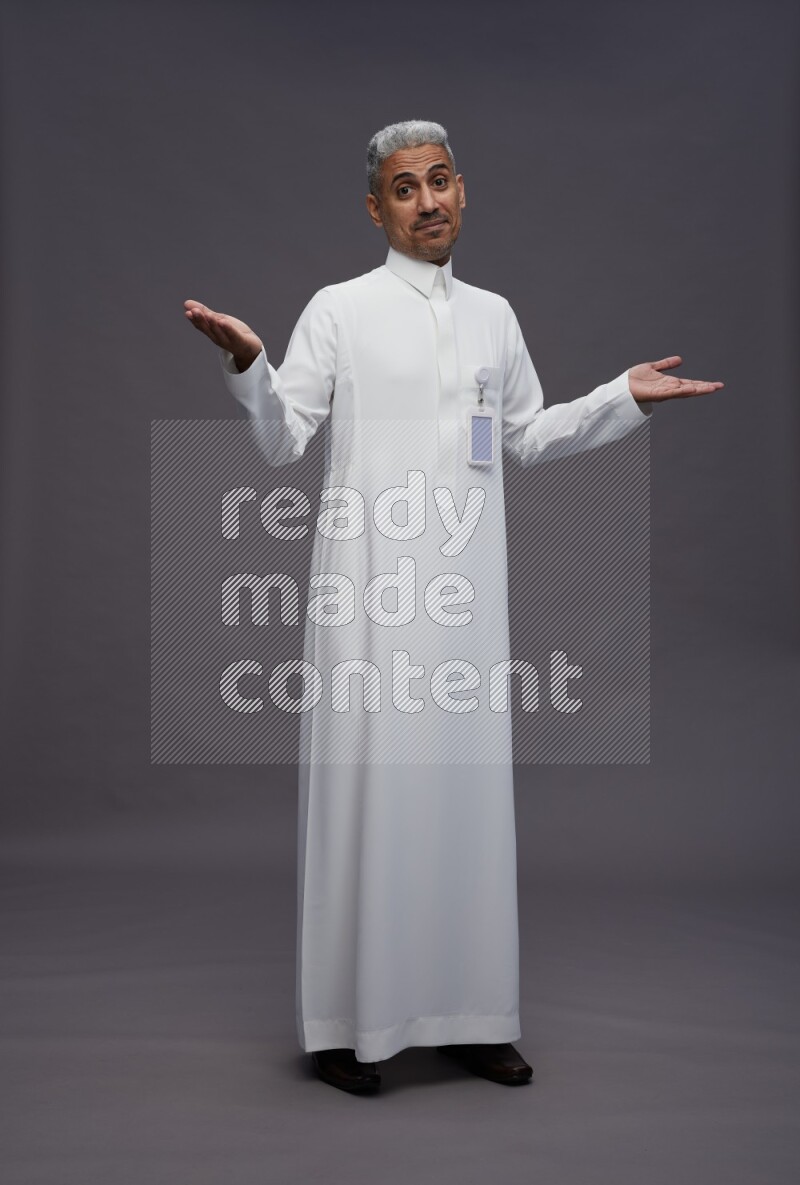 Saudi man wearing thob with pocket employee badge standing interacting with the camera on gray background