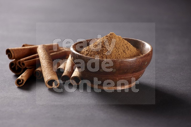 أعواد القرفة مربوطة بجانب وعاء خشبي به بودرة القرفة علي خلفية سوداء