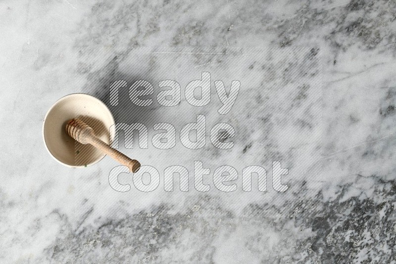 Beige Pottery Bowl with wooden honey handle in it, on grey marble flooring, Top View