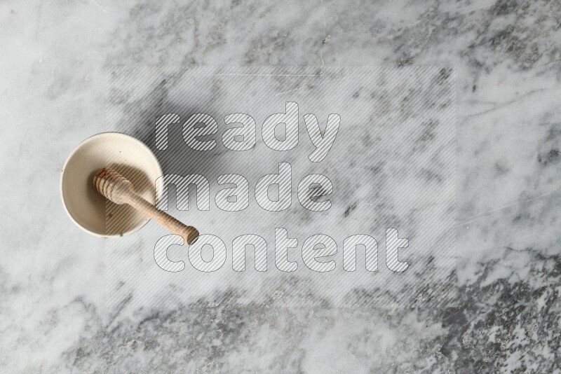 Beige pottery bowl with wooden honey dipper in it on grey marble background
