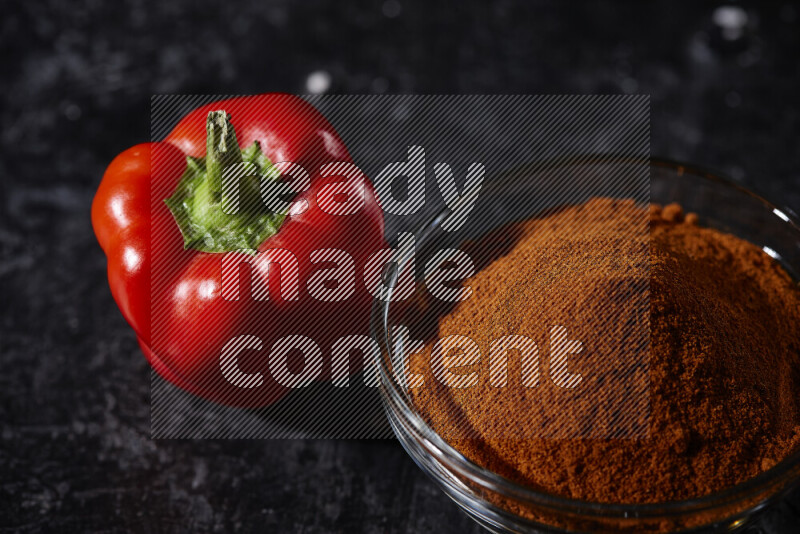 A glass bowl full of ground paprika powder on black background